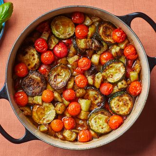 Dutch oven of ratatouille as seen from overhead with a side plate of basil leaves