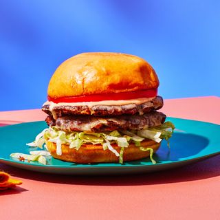 Side view of a black bean burger with two thin patties layered with shredded lettuce tomato and special sauce on a plate...