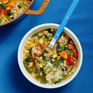 Two white bowls of minestrone alongside a large brown pot of the full yield.