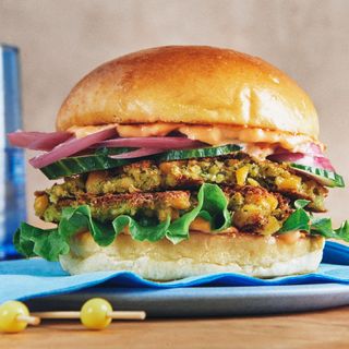 Falafel patties lettuce sliced cucumbers pickled red onions and harissa mayonnaise between two brioche buns.