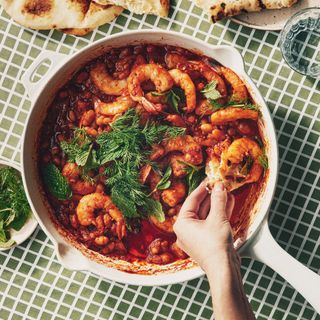 A skillet of shrimp and white beans a spicy tomato sauce topped with dill and mint and served with toasted naan.