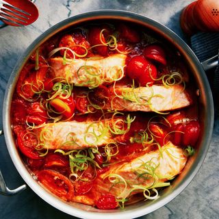 Salmon fillets tomatoes and curled scallions in a saut pan.